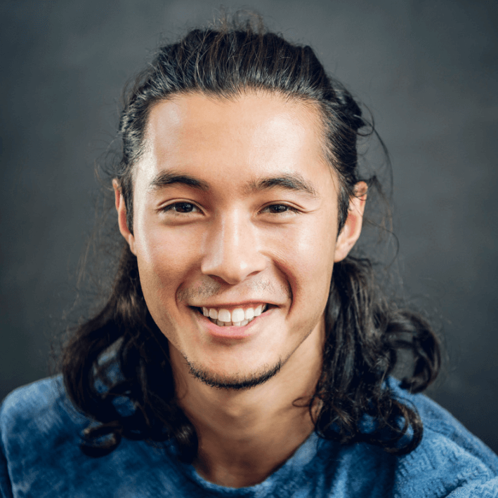 Lächelnder Mann mit langen Haaren in blauer Kleidung, der positive Ausstrahlung hat.