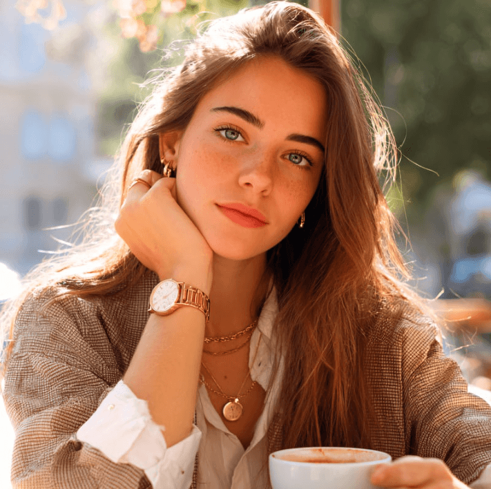 Junge Frau mit braunen Haaren und elegantem Outfit, die entspannt mit einer Tasse Kaffee sitzt.