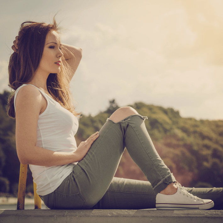 Frau sitzt im Freien und genießt die Sonne, trägt modische jeans und ein weißes Top, entspannte Pose.