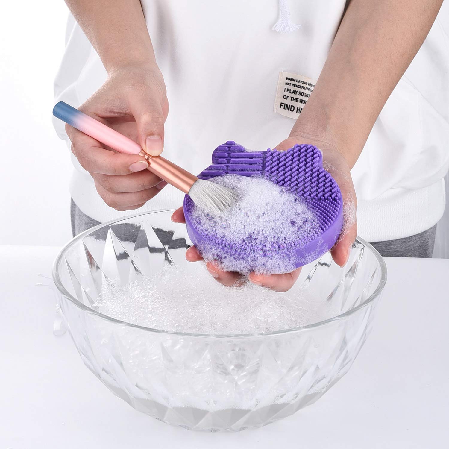 Person using Medivita Silikon-Pinselreiniger to clean makeup brush in soapy water.
