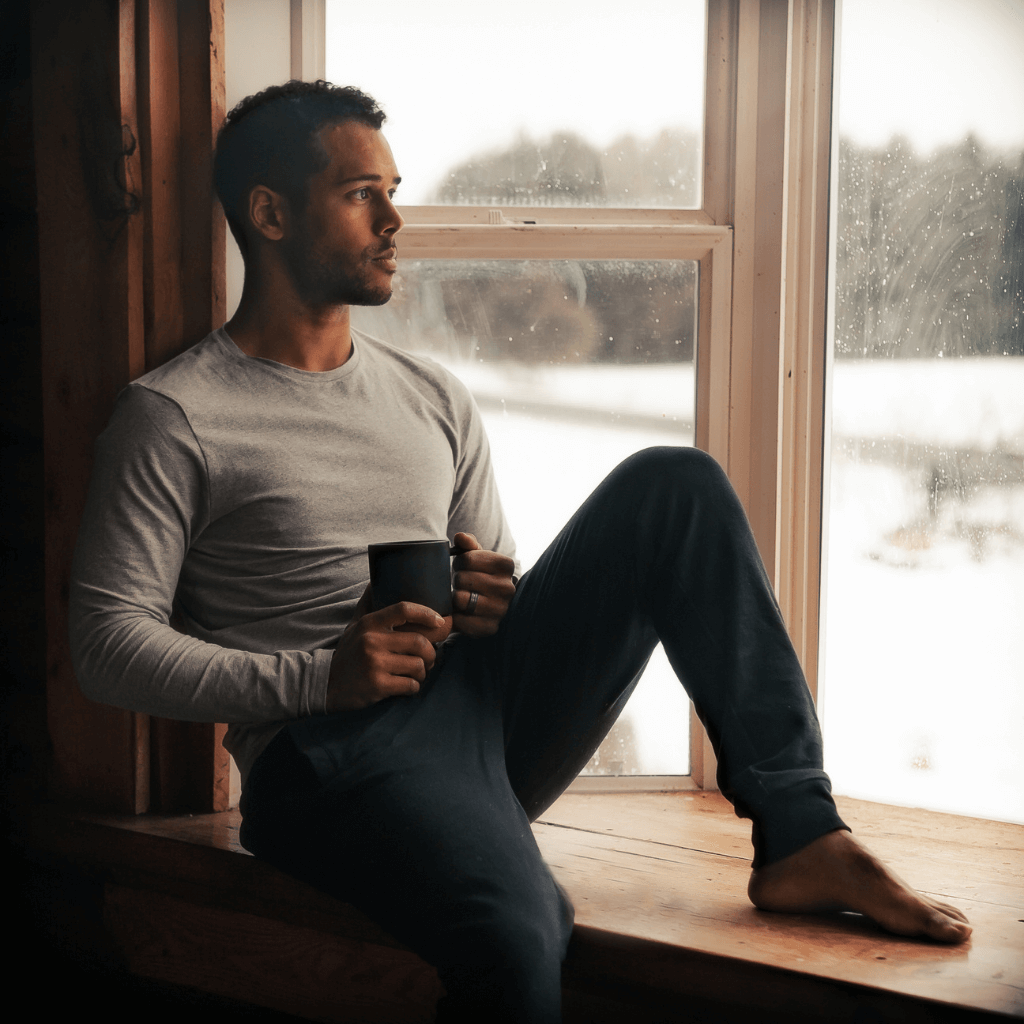 Mann sitzt am Fenster und genießt eine Tasse Kaffee während des Winterwetters.
