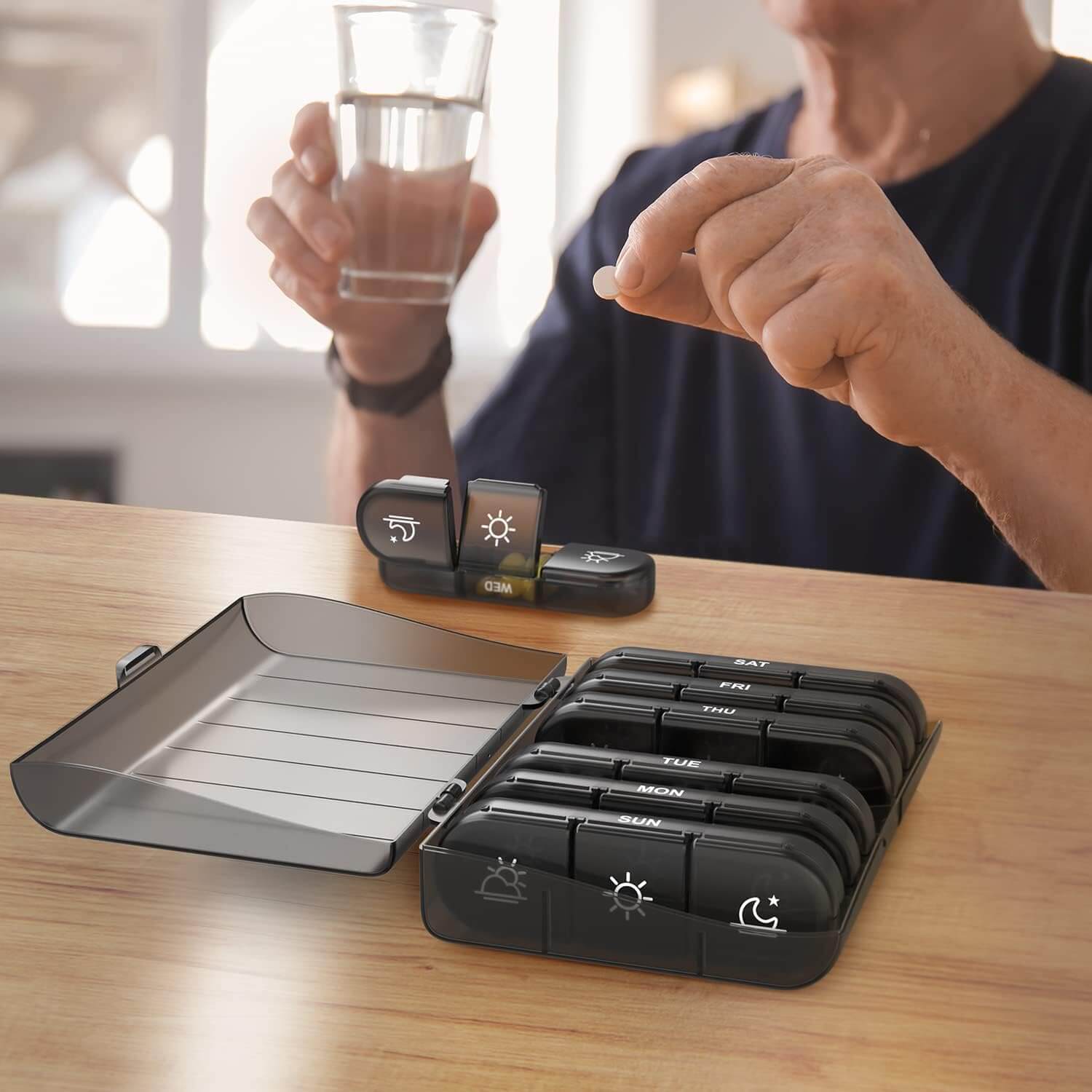 Medivita 7-Tage Pillenbox auf einem Tisch mit Medikamenten und einem Glas Wasser.